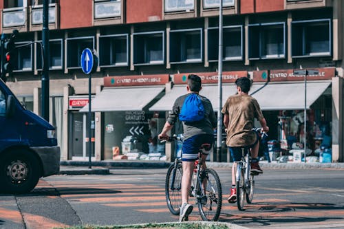 무료 빨간색과 회색 건물 근처의 도로를 여행하는 자전거를 타는 남자 스톡 사진