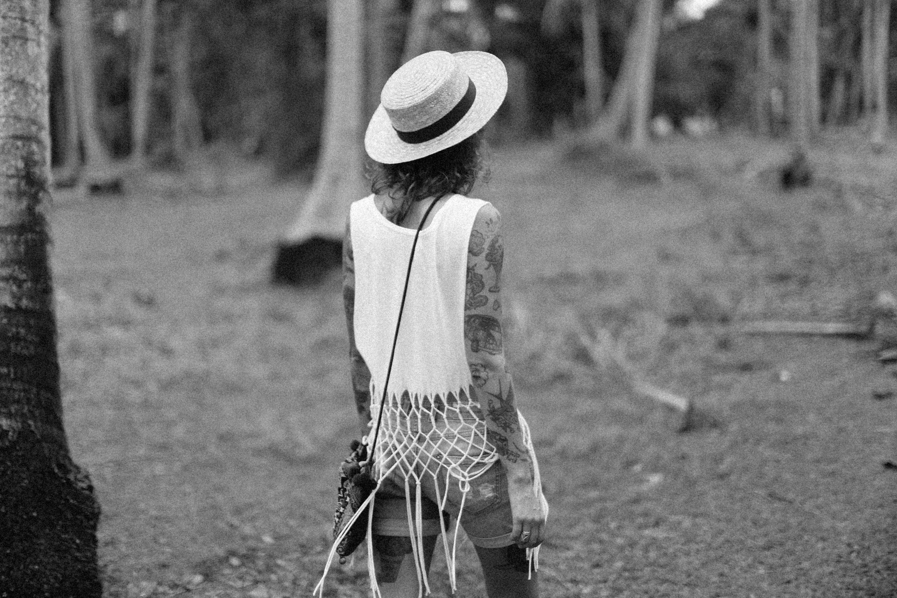 Back view of a tattooed woman in a summer outfit walking in a forest.