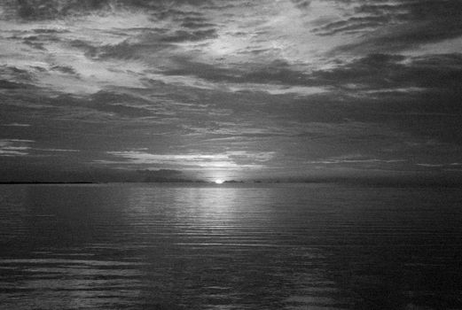 Calm sea reflecting a dramatic cloudy sunset in black and white.