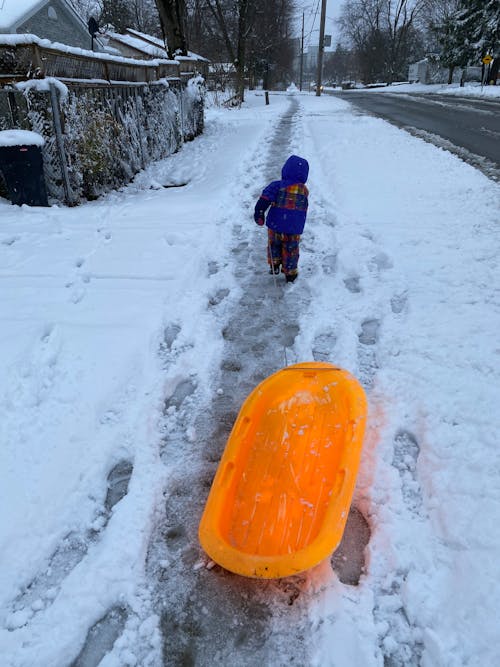 Free Back View Shot of a Kid Pulling a Snow Sled while Walking on the Snow Covered Ground Stock Photo