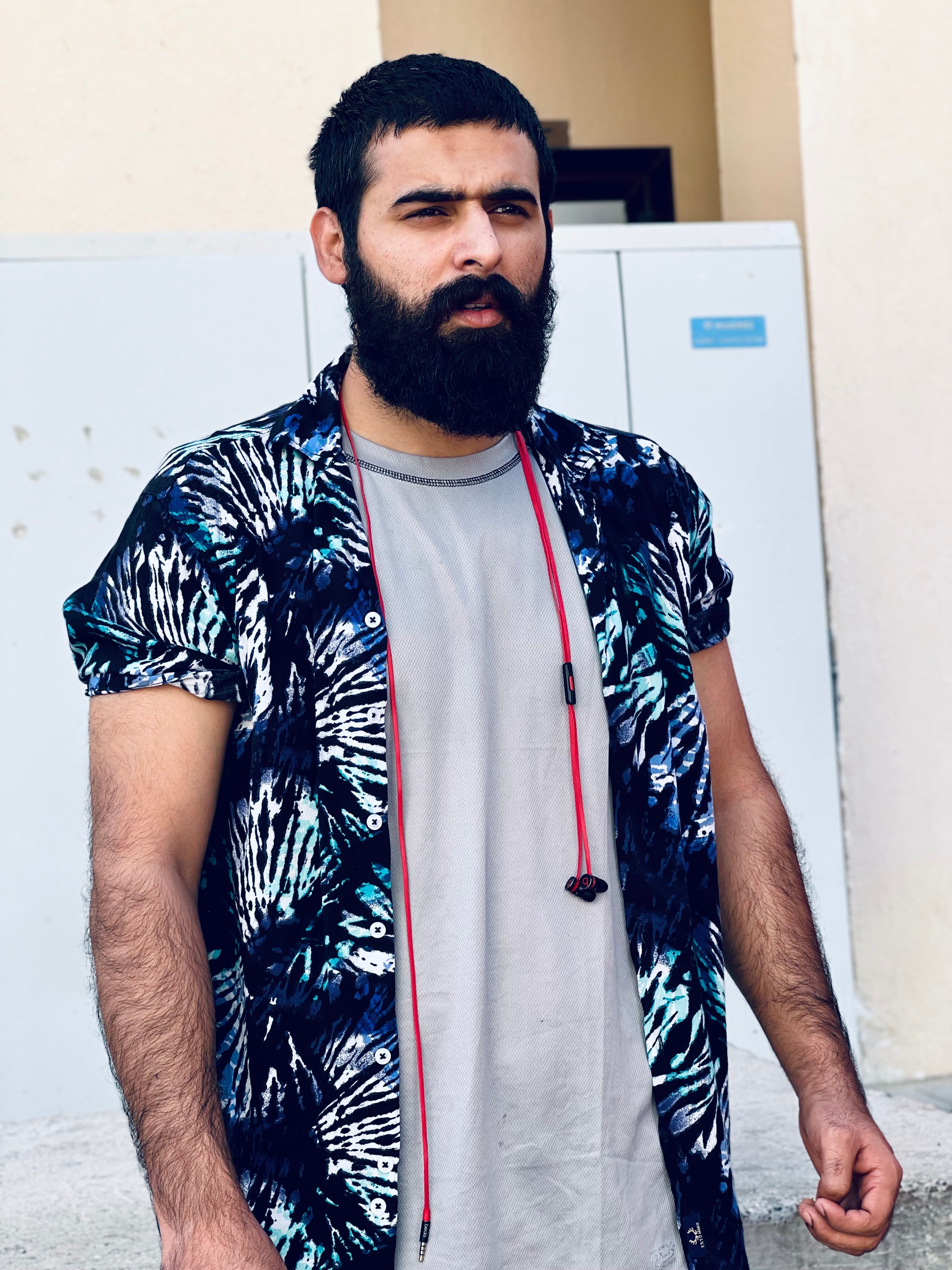 A bearded man in a tropical shirt stands outdoors, looking to the side.