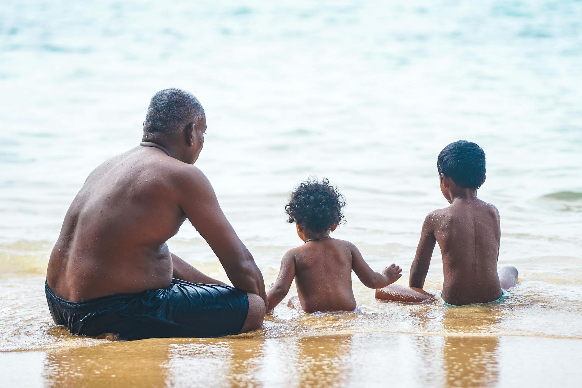 A father enjoys a bonding moment with his children at the serene beach shoreline.