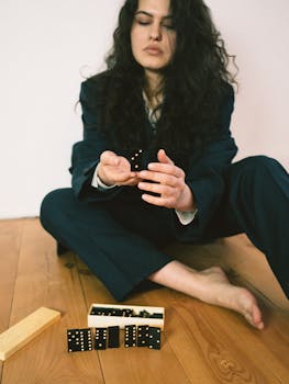 Serene woman in a suit holds domino pieces while sitting barefoot indoors.