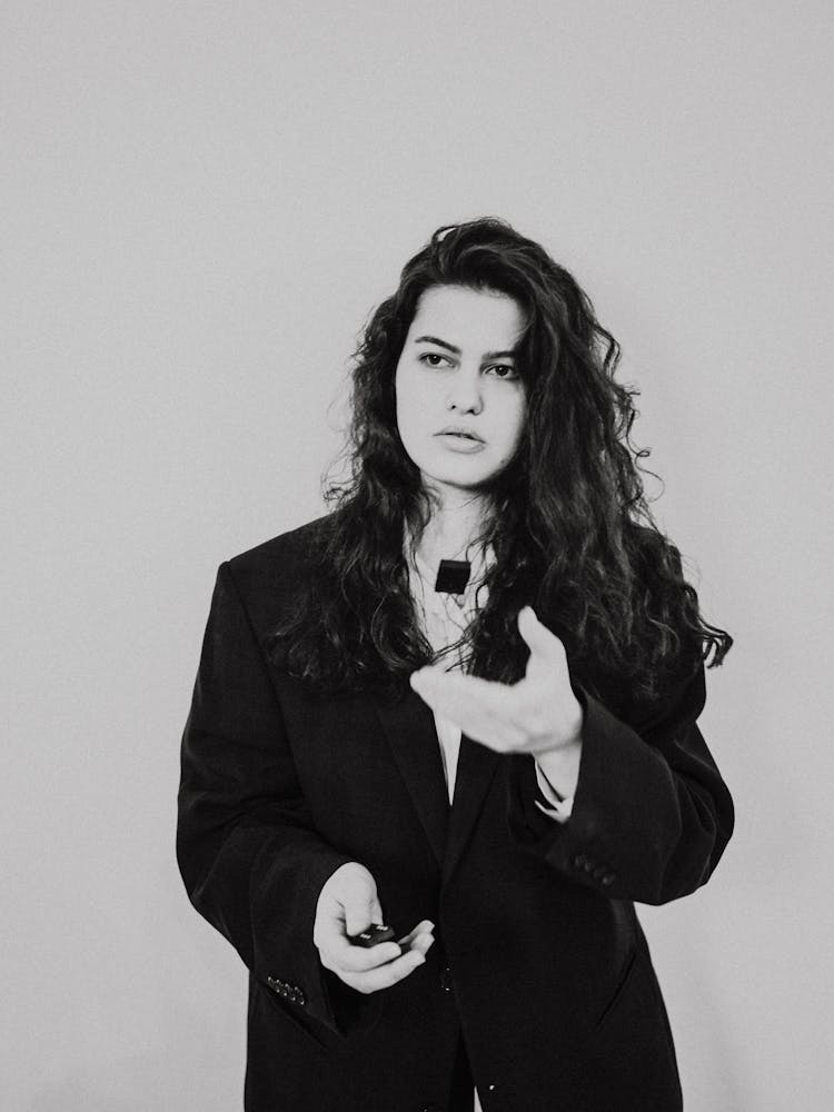 Black And White Photo Of A Woman In A Suit Giving Presentation