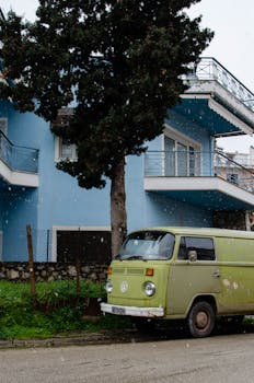 A retro green van parked by a blue building under snowfall, capturing a nostalgic urban scene.