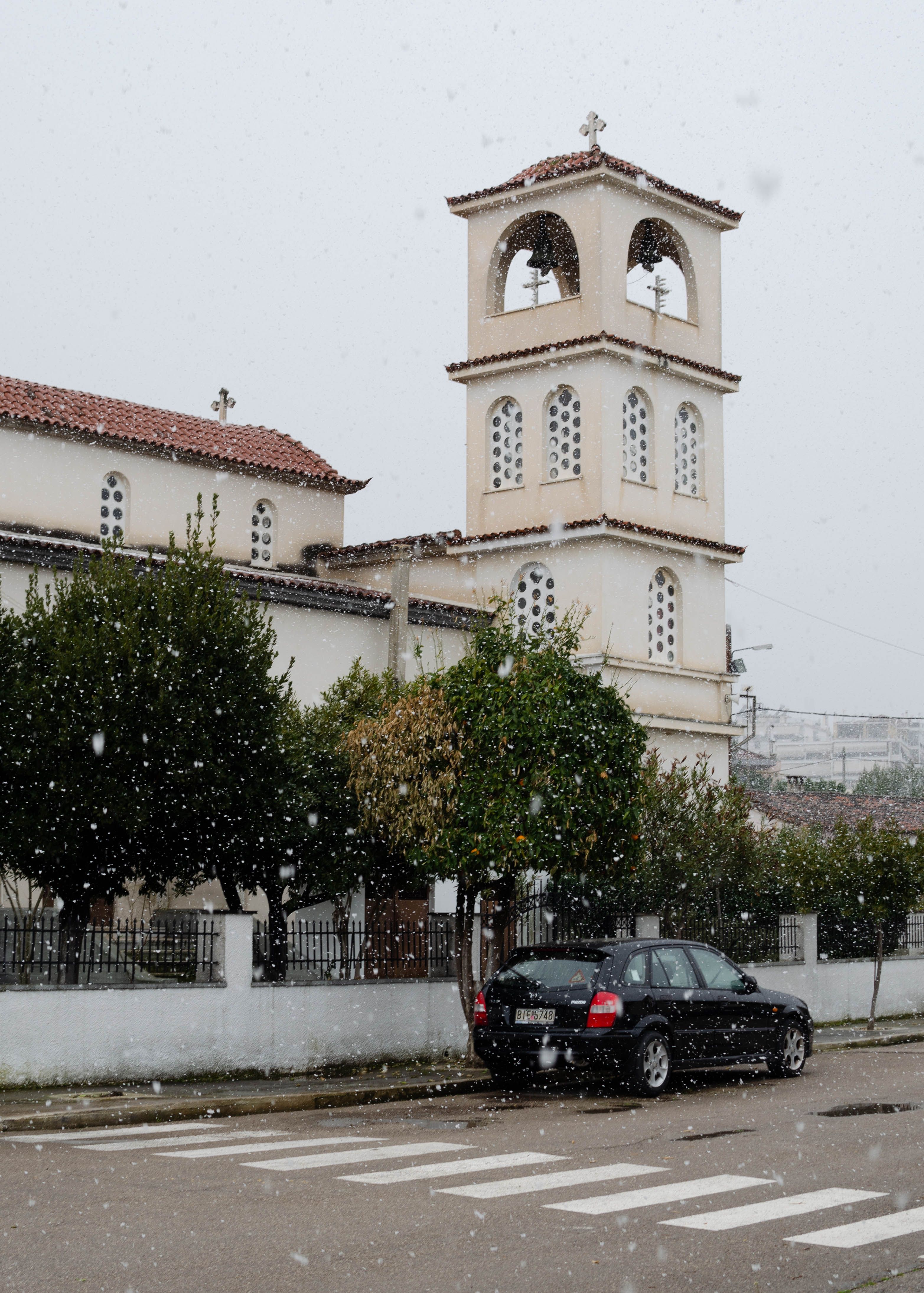 A black car parked in front of a church during snowfall, emphasizing tranquility.