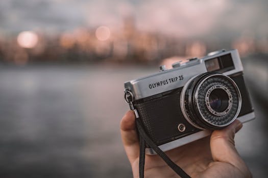 A hand holding an Olympus Trip 35 camera with Istanbul skyline in the background.