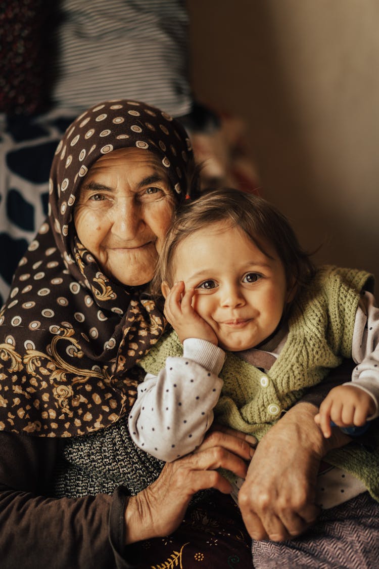 Elderly Woman In Kerchief On Head Holding Child On Her Lap