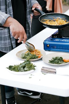 Close-up of outdoor cooking with pasta and fresh greens on ceramic plates.