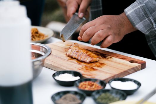 Chef preparing a meal with grilled chicken, herbs, and spices on a wooden cutting board.