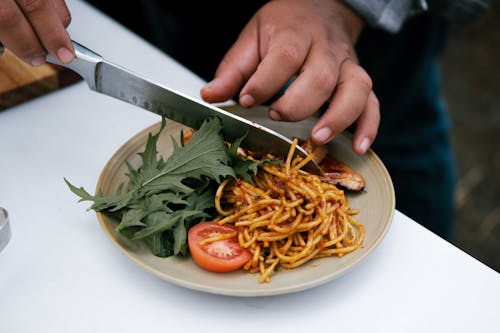 A Hand Preparing the Pasta with Red Sauce on a Ceramic Plate