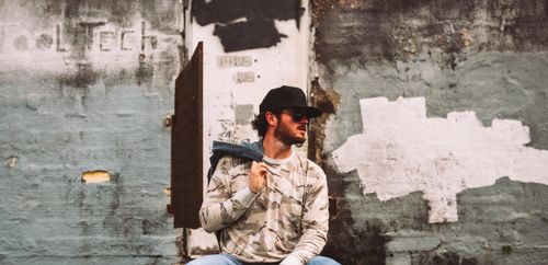 Free Fashionably dressed man sitting against a grungy urban wall. Stock Photo