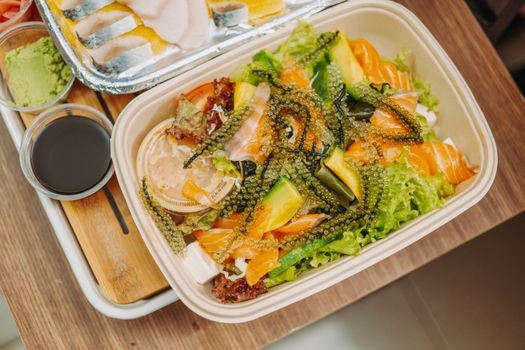 Delicious seafood salad with fresh seaweed, avocado, and salmon in a biodegradable container.