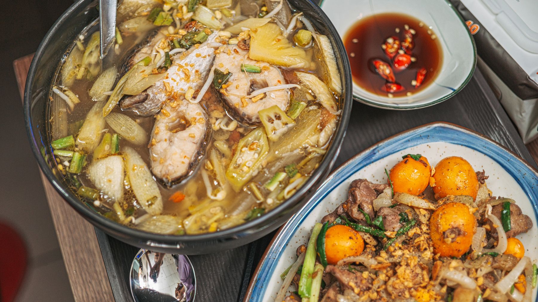 Close-up of a hearty Vietnamese meal featuring fish soup and a savory side dish garnished with greens and spices.