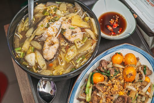 Close-up of a hearty Vietnamese meal featuring fish soup and a savory side dish garnished with greens and spices.