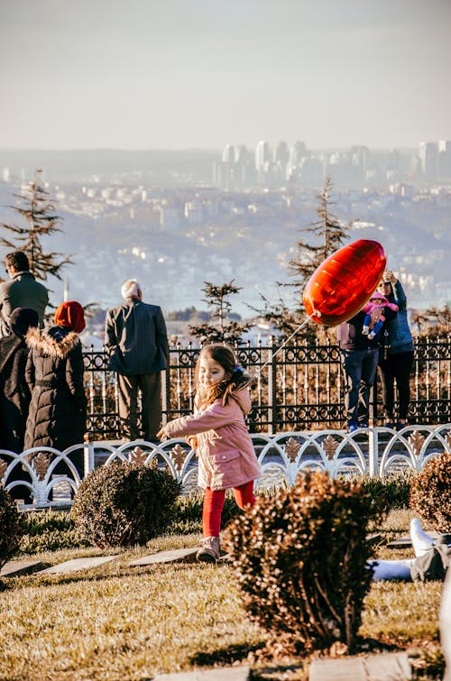 A Girl Running in the Park while Holding Red Heart Shaped Balloon