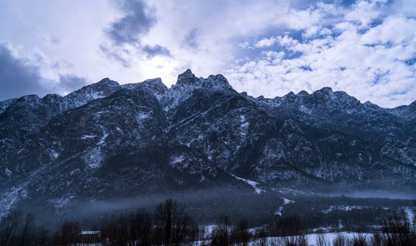 Majestic snow-covered mountains in winter at Ospedaletto, Italy under a cloudy sky.