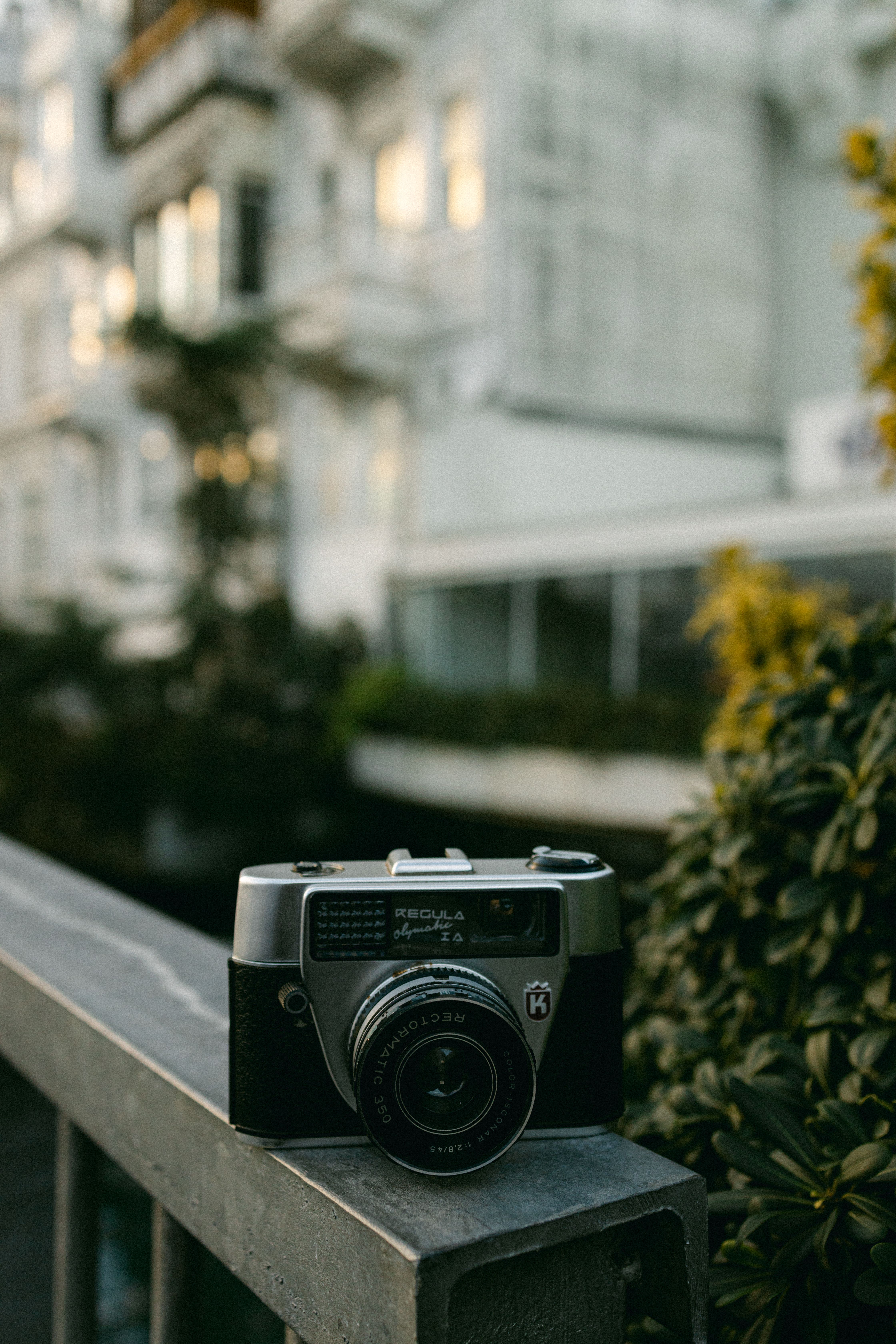 Close-up of an analog camera on a balcony rail, with a blurred building background.
