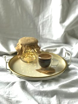 Glass coffee cup and decorative light jar on a tray against a soft backdrop.