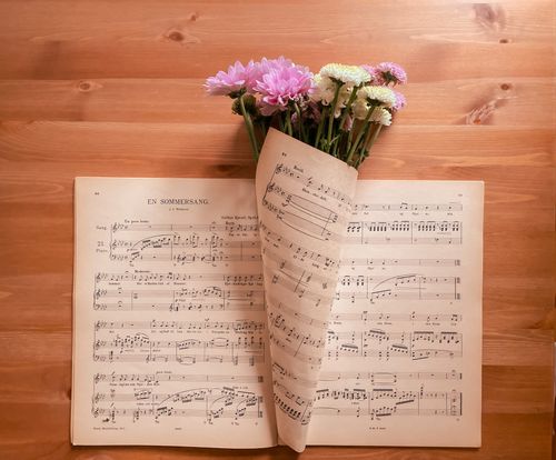 Free A lovely floral bouquet placed on open sheet music over a wooden table, creating a harmonious blend of nature and art. Stock Photo