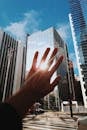 一只手伸向现代玻璃摩天大楼，它在充满活力的城市环境中反射着阳光