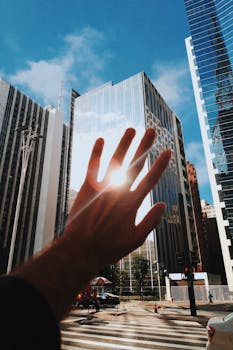 一只手伸向现代玻璃摩天大楼，它在充满活力的城市环境中反射着阳光