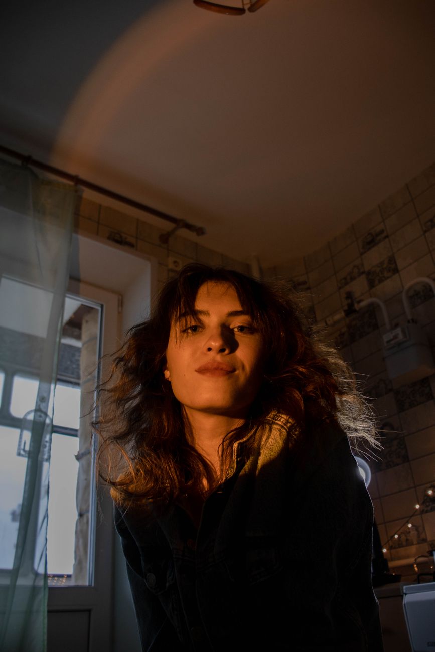 A woman poses in a warmly lit apartment interior, creating a moody ambiance.