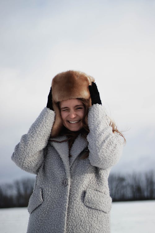 Smiling Woman in Warm Coat Holding Fur Hat on Head 