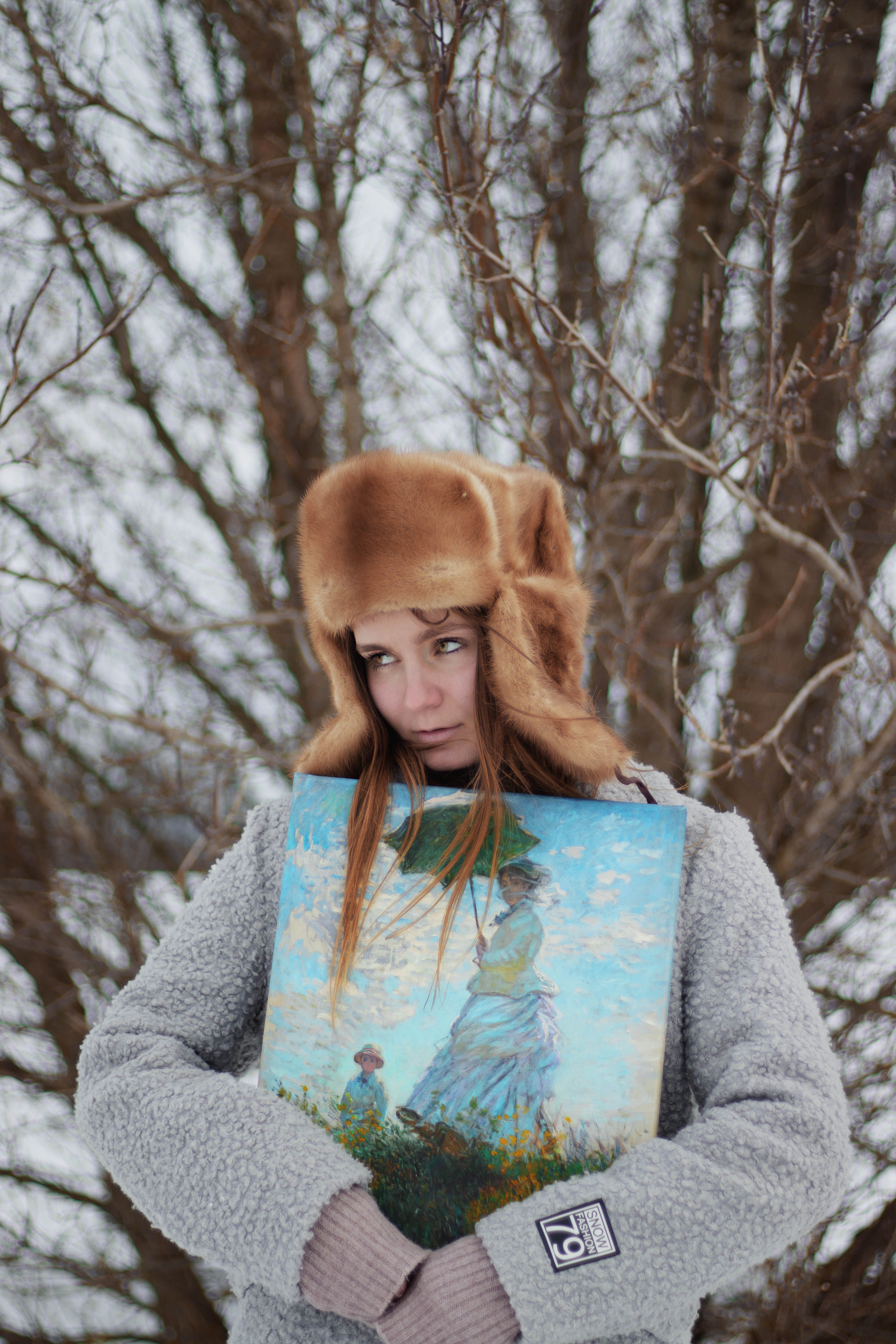 Young woman in a fur hat holding art in a snowy outdoor setting.