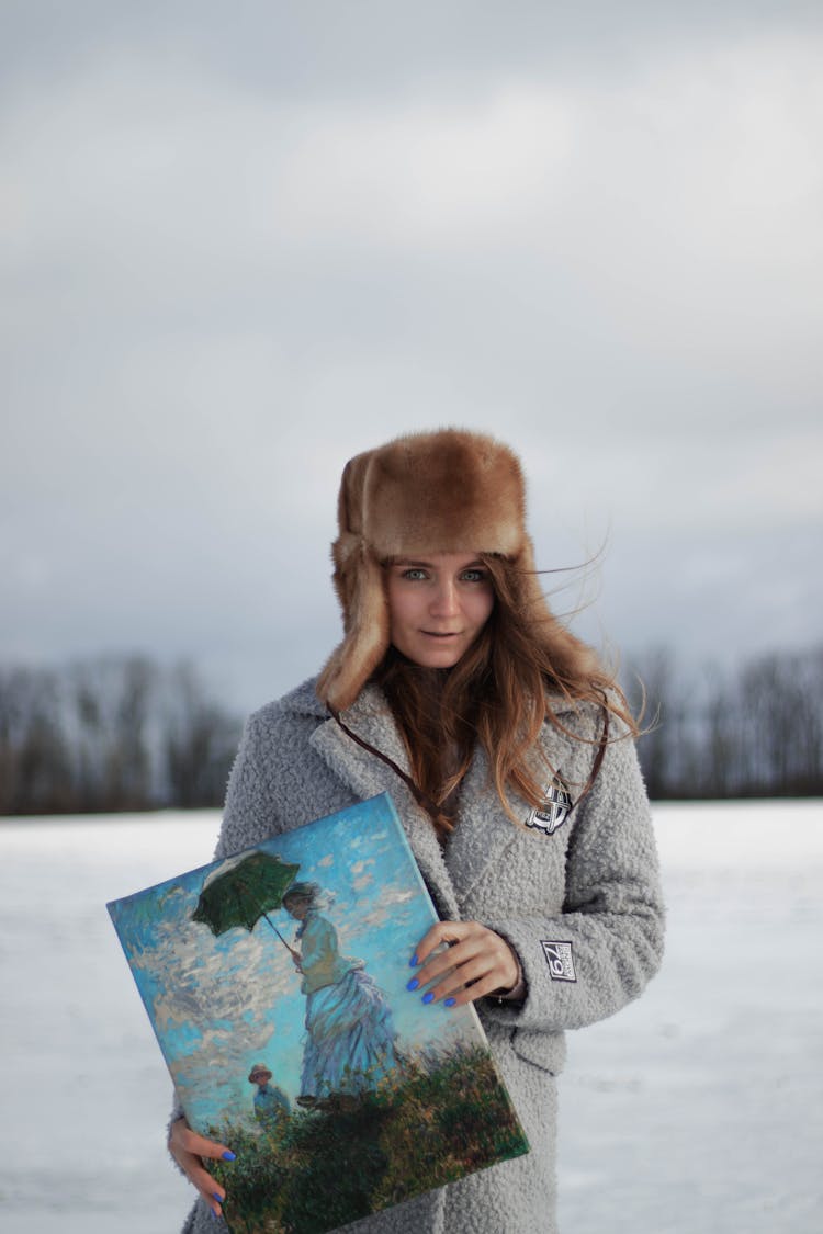 Woman With Painting Wearing Warm Clothing On Winter Landscape