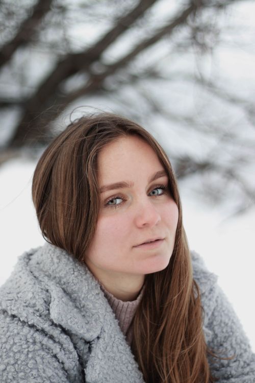 Free Captivating winter portrait of a woman dressed warmly in a fluffy coat against a snowy backdrop. Stock Photo