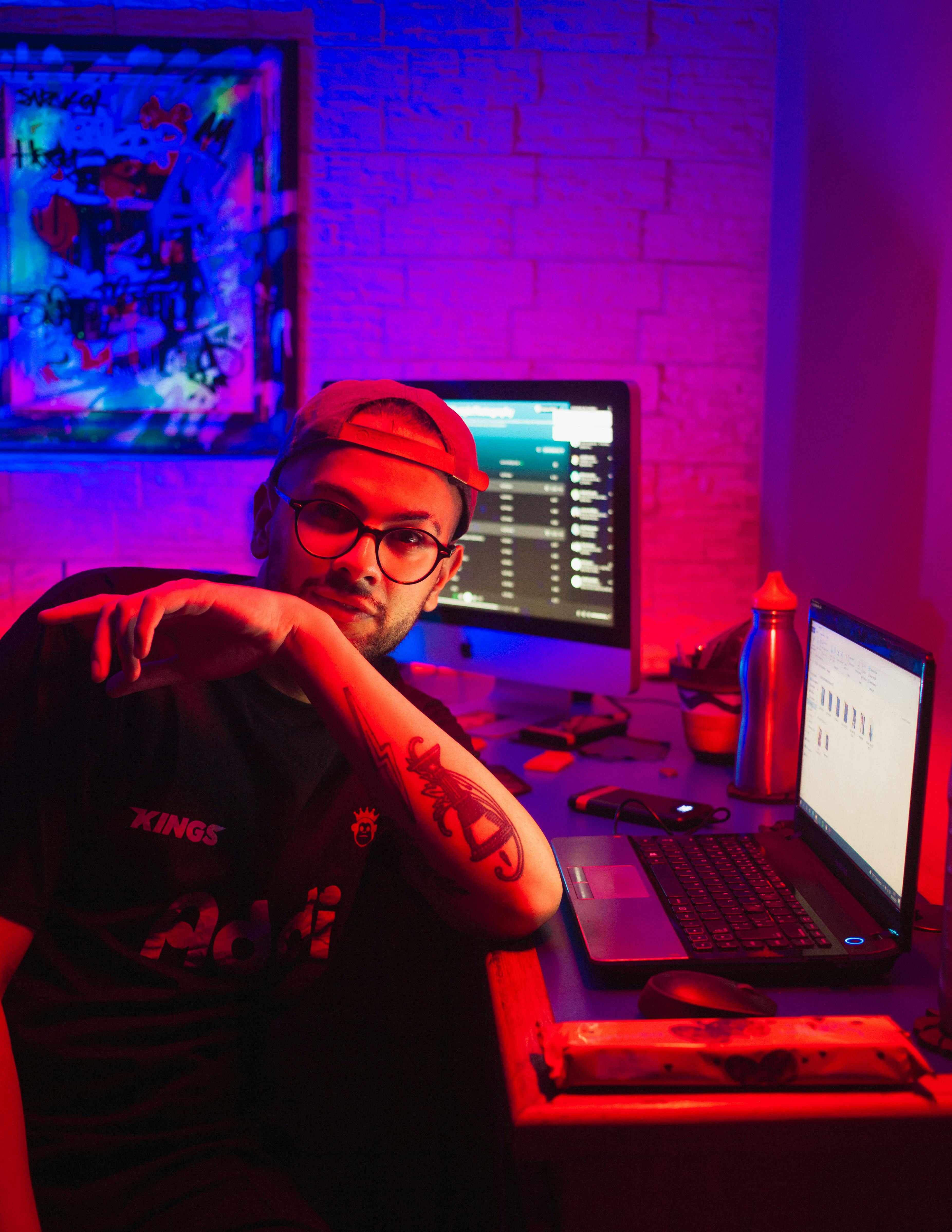 A man sitting at a desk with illuminated screens in a neon-lit room.
