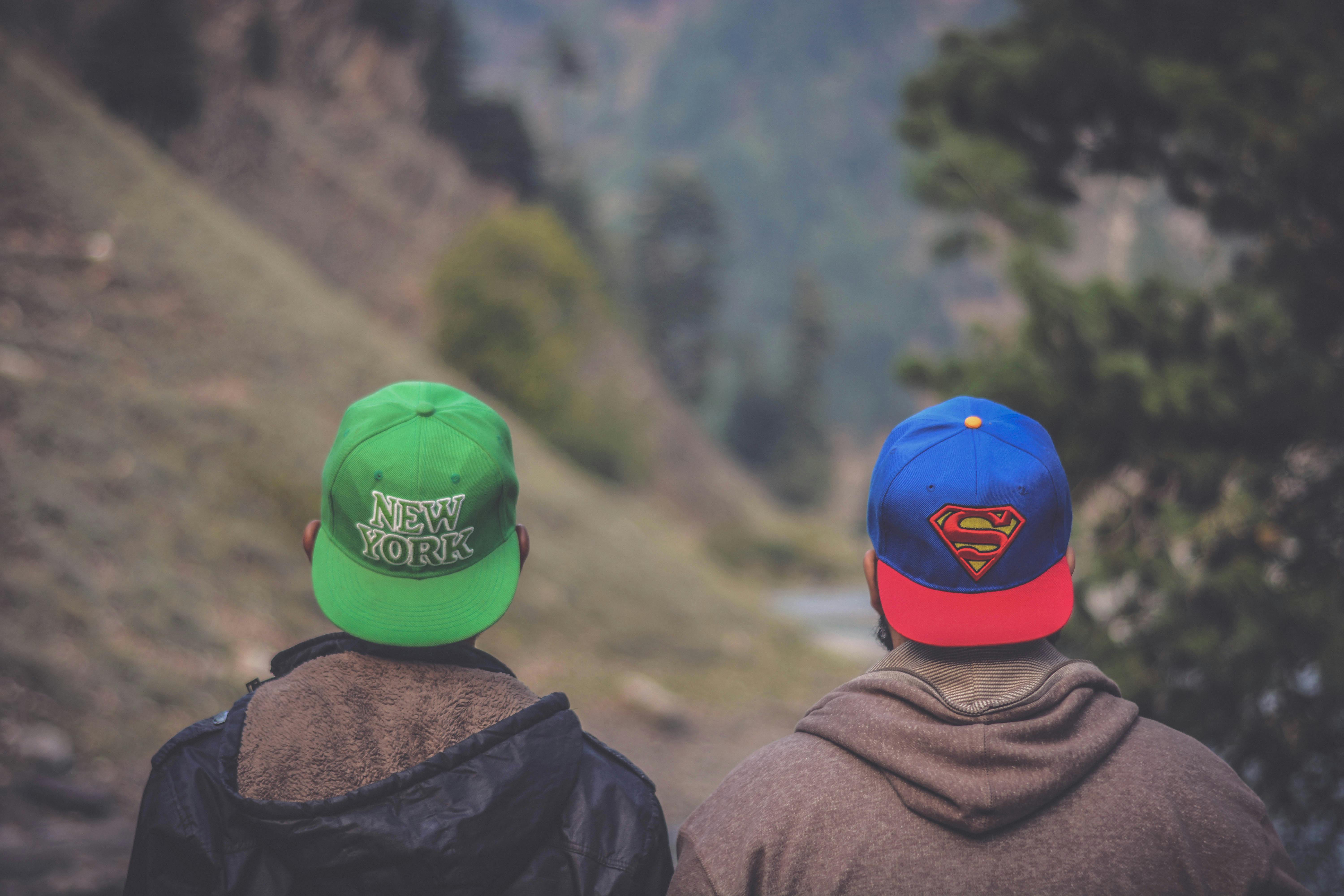 Back view of two friends wearing caps in a scenic outdoor landscape setting.