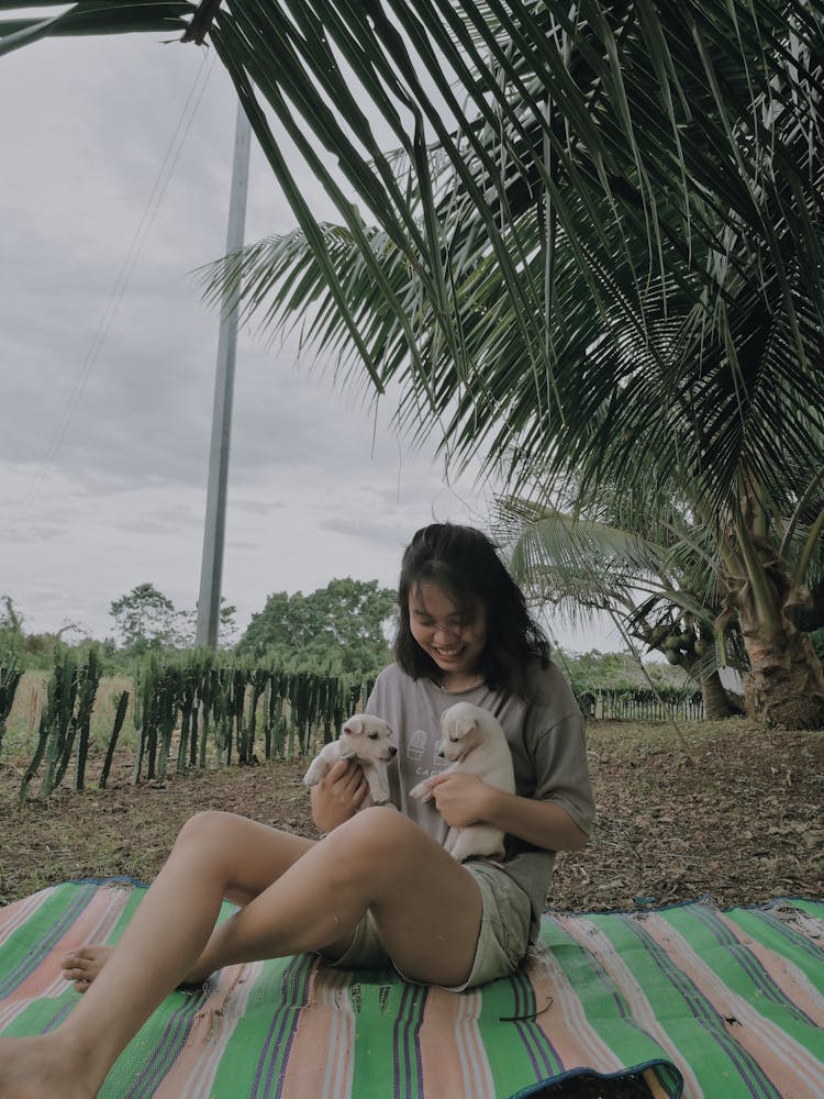 Woman Sitting On Blanket Holding Puppies