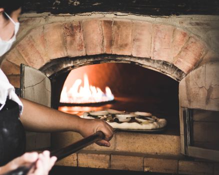 Close-up of a chef placing pizza in a traditional wood-fired oven.