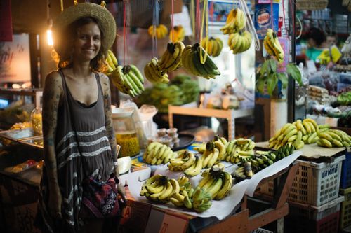 Free Smiling woman in straw hat at a lively market banana stall, showcasing fresh produce and vibrant atmosphere. Stock Photo