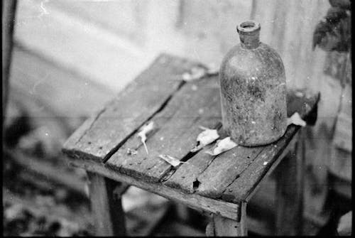 Black and White Photo of a Bottle on a Weathered Stool