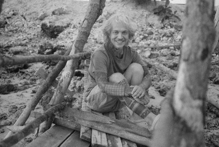 Smiling Young Man Sitting On A Wooden Construction 