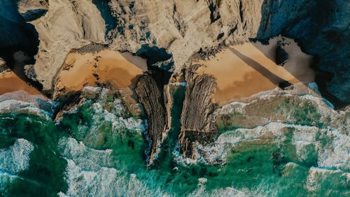Free Aerial image capturing rugged cliffs, beach sands, and turquoise waves in a coastal setting. Stock Photo