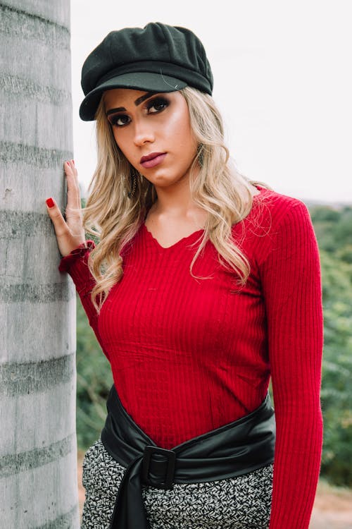 Free Woman Wearing Black Cap and Red V-neck Sweatshirt Near Concrete Wall Stock Photo