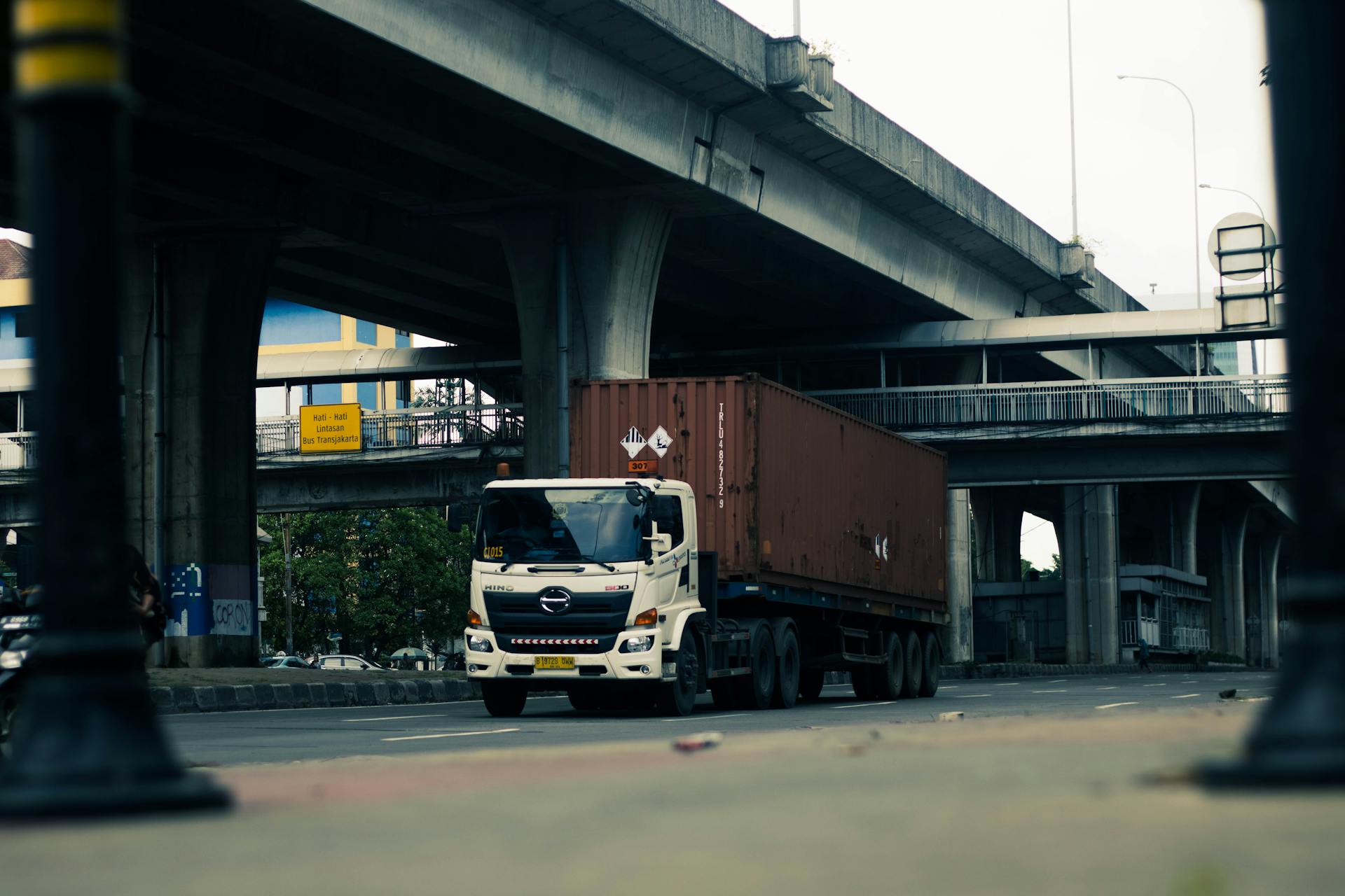 White cargo truck driving under city overpass in Jakarta, showcasing urban transportation.