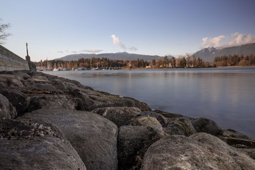 Peaceful lakeside scene with rocky shore, calm water, and distant mountains under a clear sky.