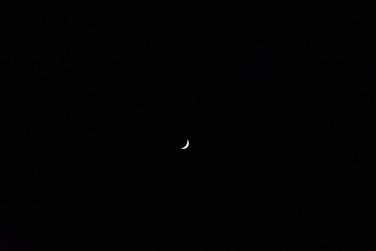 a serene crescent moon floating in a vast and dark night sky creating