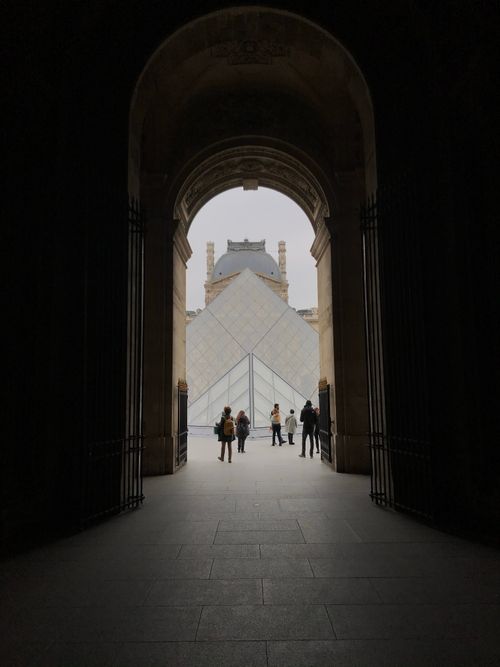Free View of the Louvre Pyramid through a grand archway in Paris, capturing a blend of historic architecture. Stock Photo