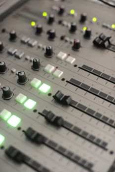 Detailed view of the control panel on a professional audio mixer, highlighted by glowing LED lights.