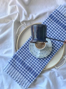 Artistic overhead shot of coffee brewing with blue tones and ceramic cup on checkered cloth.