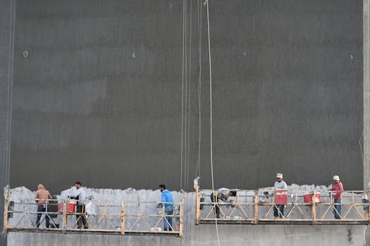 Workers on a suspended platform renovating a building facade, showcasing teamwork and urban development.