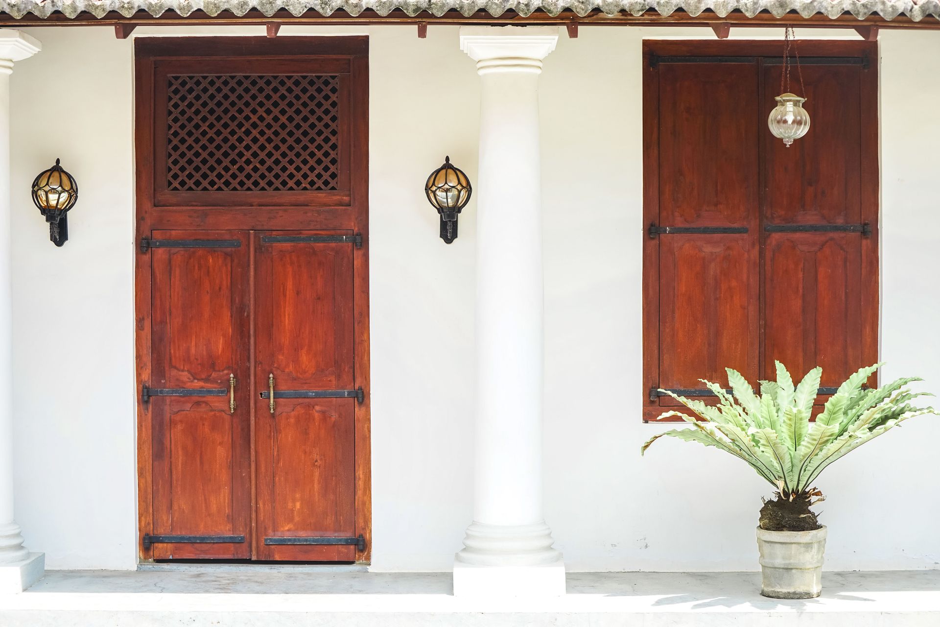 Elegant wooden door with vintage sconces beside a potted fern, perfect for a rustic aesthetic.