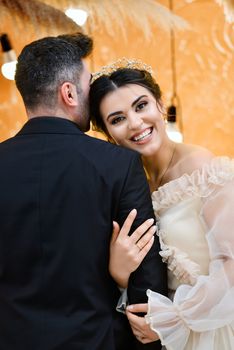 Bride smiling joyfully while embracing groom in a warm and elegant indoor setting.