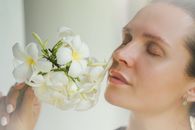 Close-up portrait of a woman holding white frangipani flowers with eyes closed, depicting serenity and natural beauty.